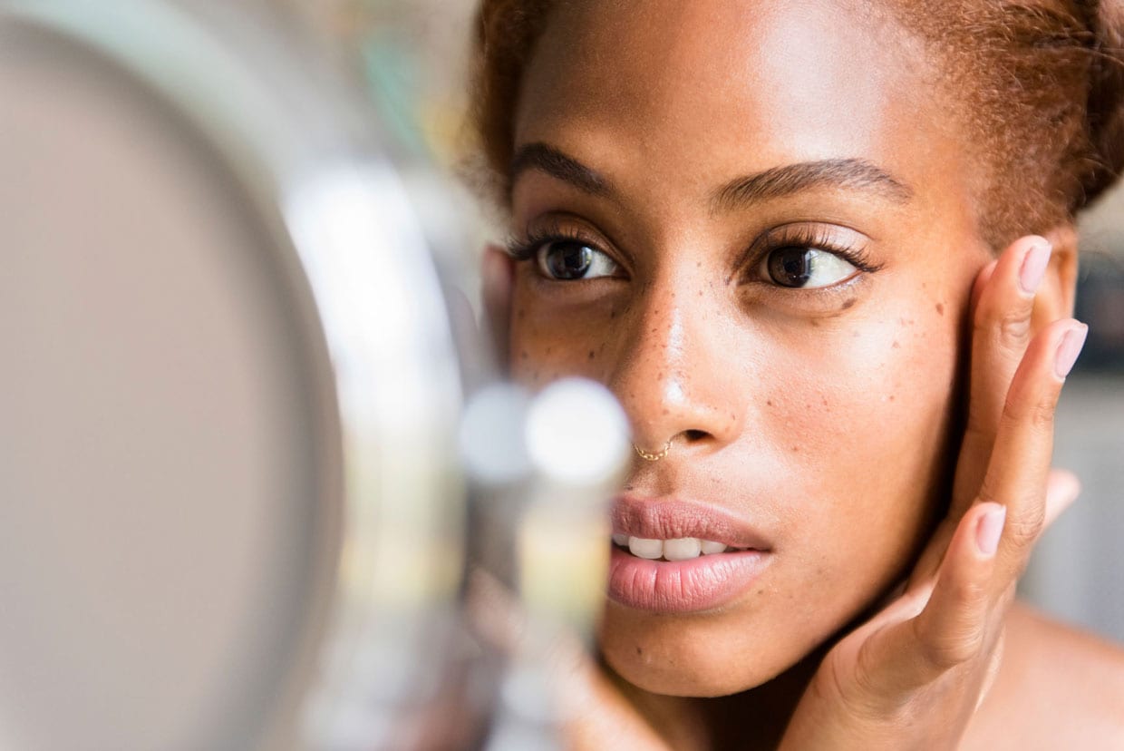 A woman looks at her skin in a mirror.