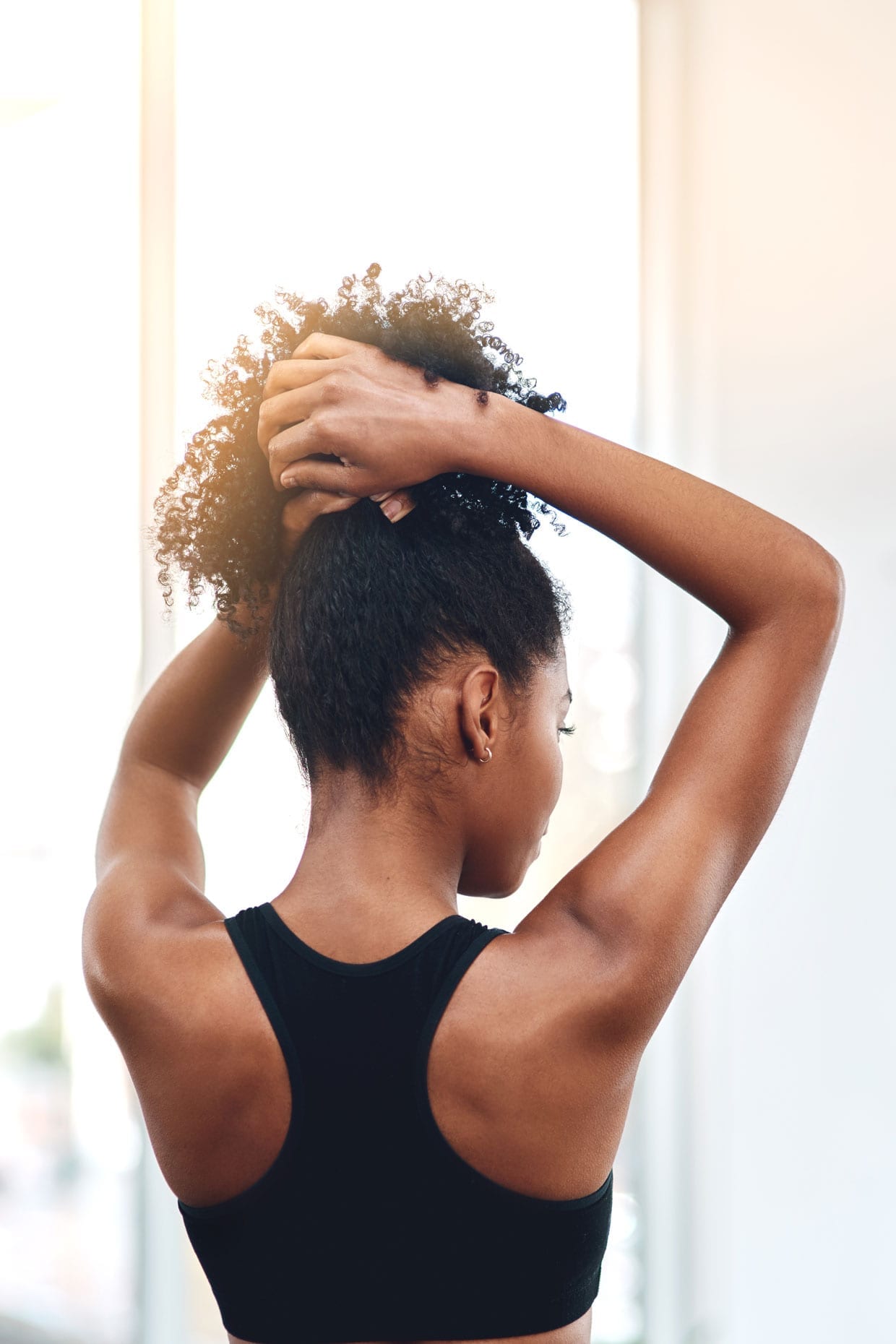 A black woman pulls up her hair into a ponytail.