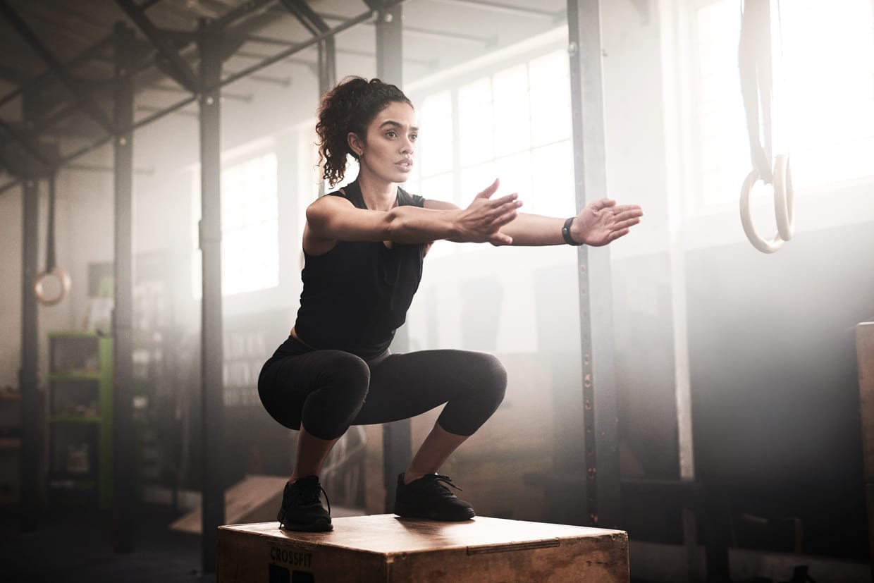 A woman performing a box jump in a gym.