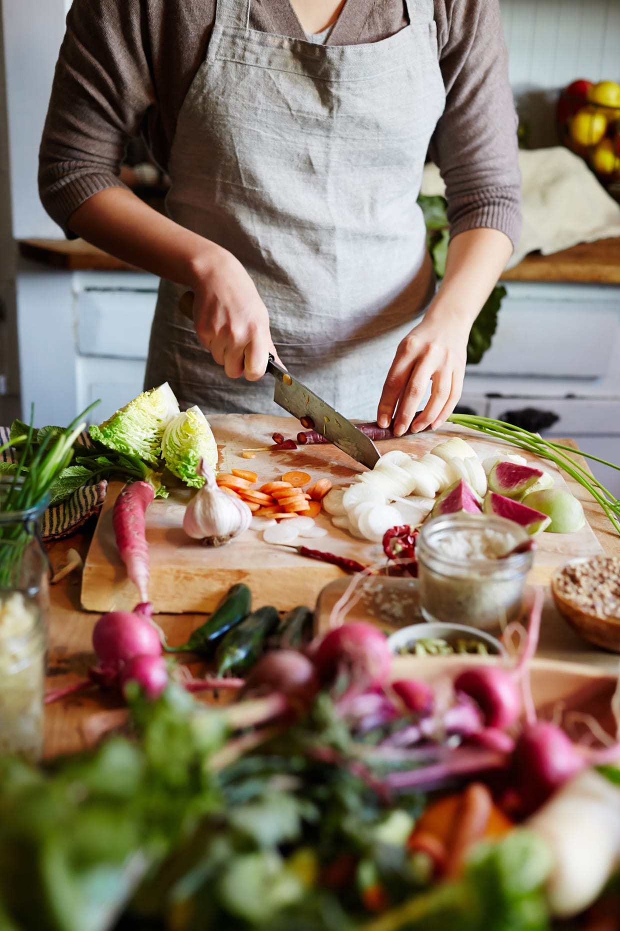 Woman wearing an apron slicing vegetables on a chopping board.