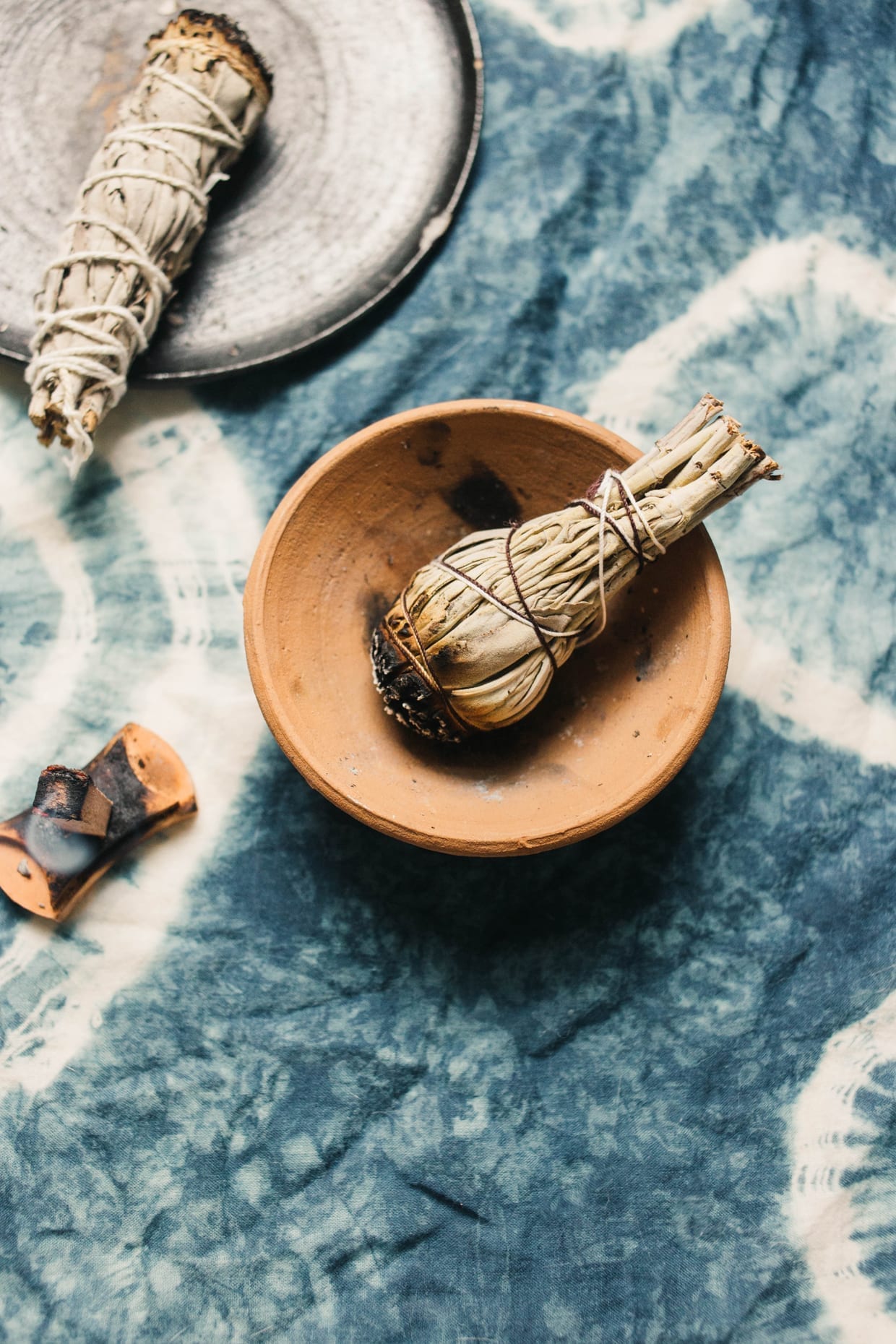 Burning sage in a bowl on a blue and white tie-dye blanket.