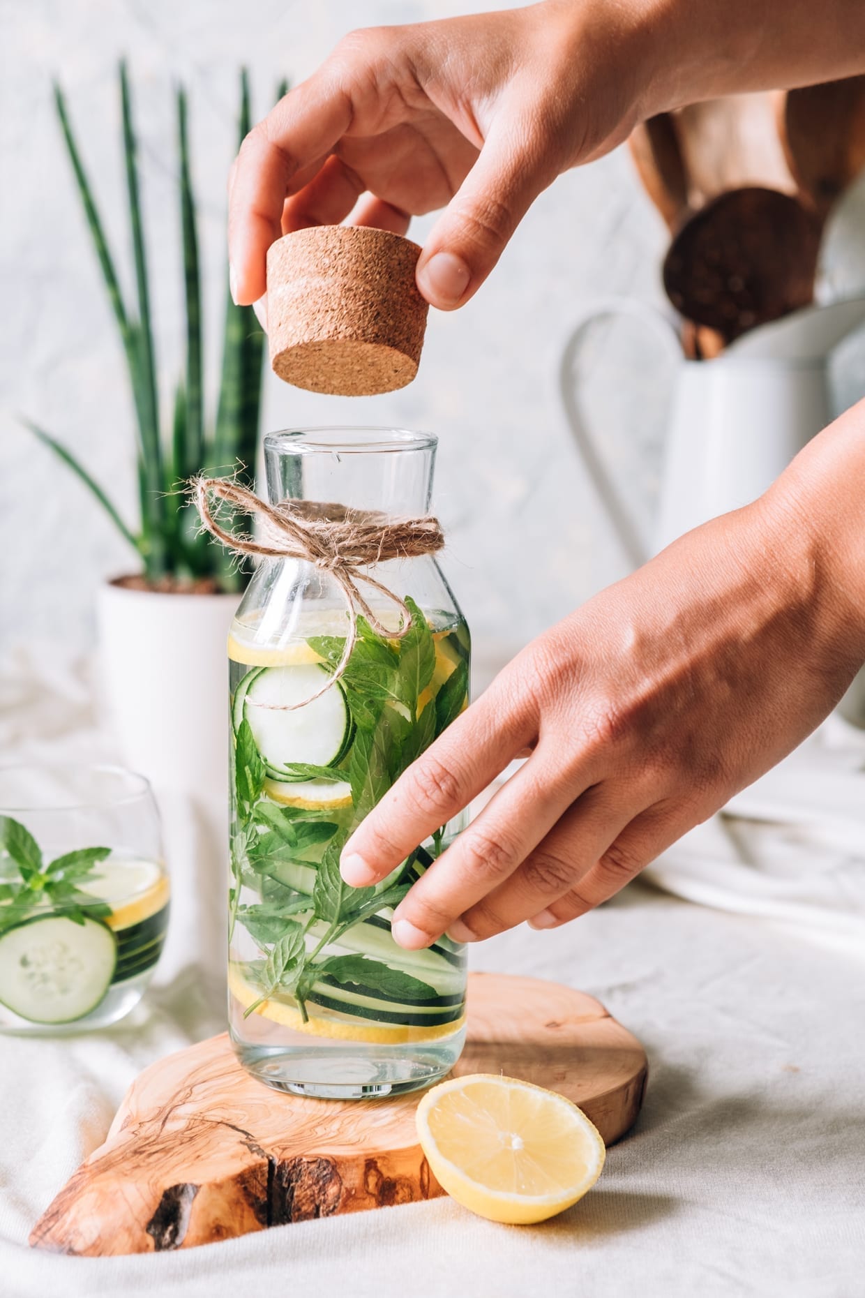 Hands opening a detox drink with cucumber, fresh mint and lemon.