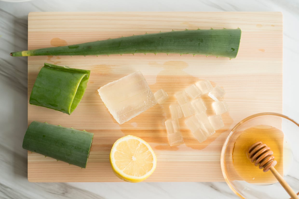 An overhead shot of aloe vera, honey and lemon on a cutting board.