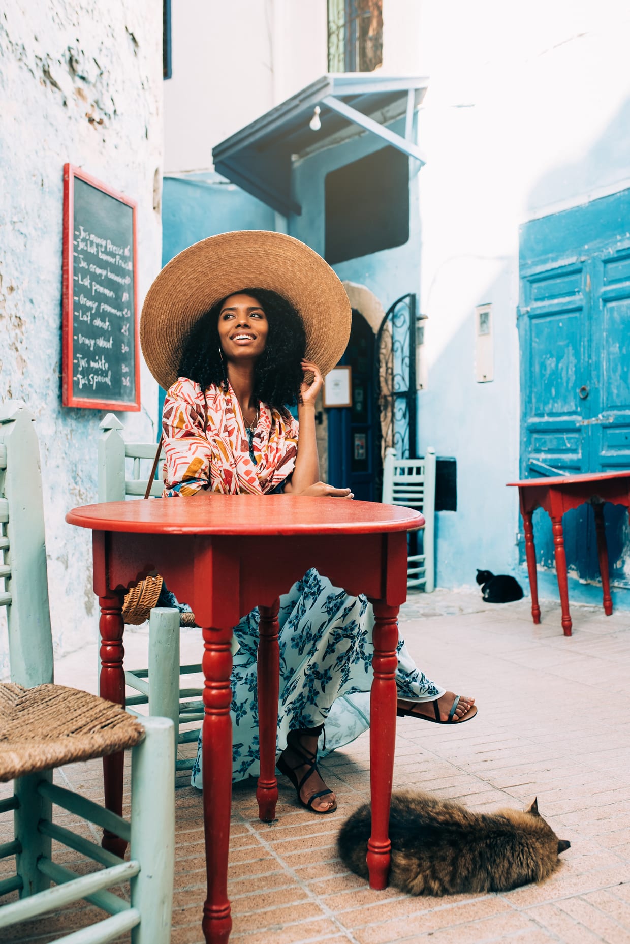 A Black woman sitting outside a coffee shop with straw hat.